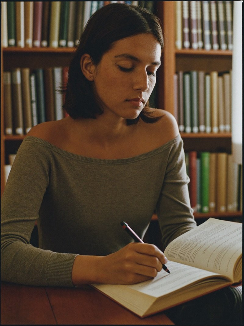 Alumna tomando notas sobre un libro en la biblioteca del instituto